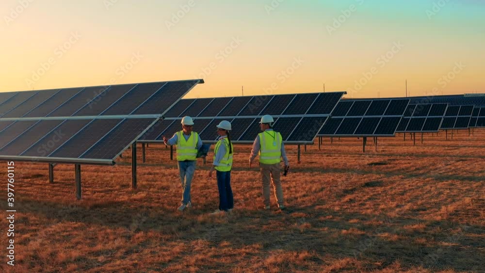 Solar energy industry workers observing a large solar farm at sunset. Professional engineers discuss innovative project.
