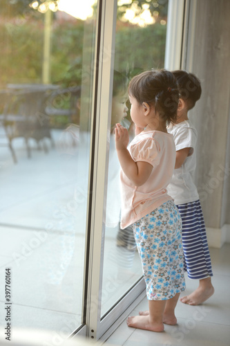 asian little boy and girl looking outside through the window