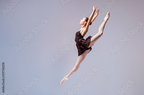 A young ballerina in a black swimsuit and pointes jumps against a bright background.
