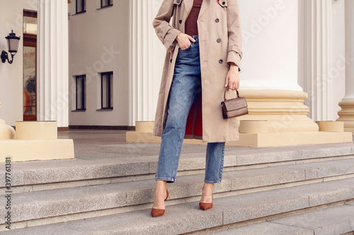 Fashion model woman in beige coat and jeans with brown mini bag on the stairs