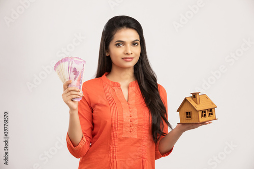 Photography Cute Indian woman holding an house model and Indian money model on white