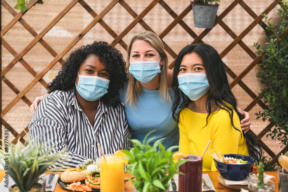Multiracial friends wearing face mask while having healthy lunch in coffee brunch bar during corona virus pandemic