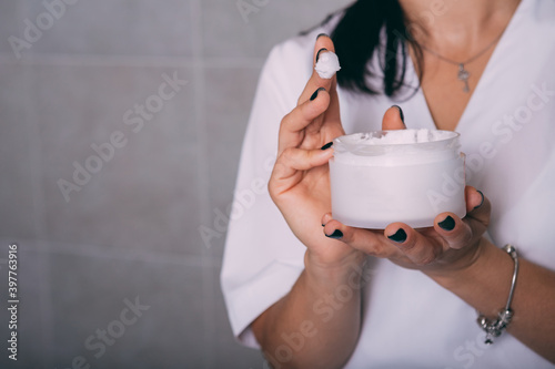 A jar of cream in the hands of a beautician. Open jar with face care cream in the hands of a girl beautician, close-up with a place for text