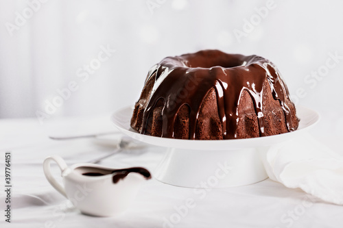 Dark chocolate cake covered with icing on a white stand. Selective focus.