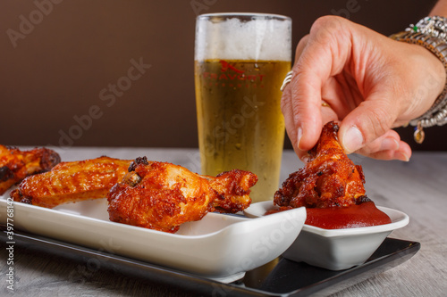 Aletta di pollo fritta e speziata con un boccale di birra sullo sfondo mentre viene immersa nella salsa bbq  photo