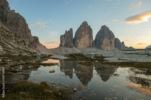 Golden hour over the Tre Cime di Lavaredo (Drei Zinnen), mountains in Italian Dolomites. The peaks reflect in a paddle. The mountains are surrounded with orange and pink clouds. Sunset time. Serenity