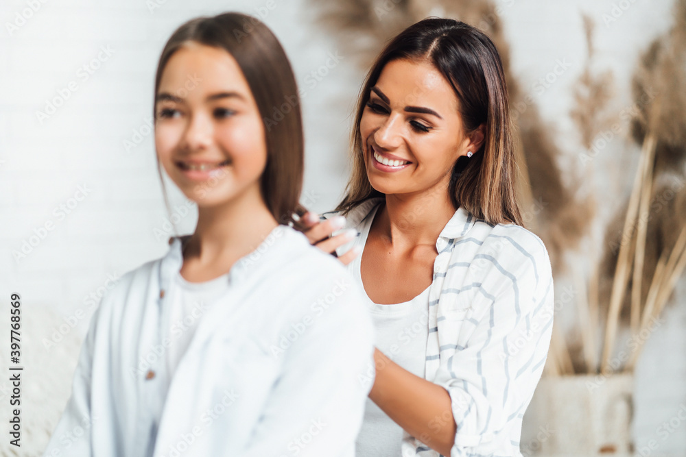 A beautiful young and happy mother braids her daughter's hair A beautiful young and happy mother braids her daughter's hair