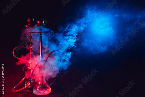 Modern hookah, shisha on a smoky black background with neon lighting and smoke. Place for your text photo