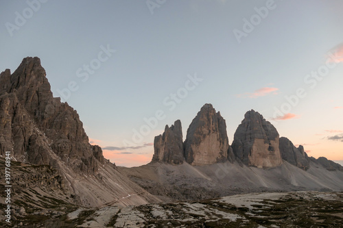 A panoramic capture of the sunset above Tre Cime di Lavaredo  Drei Zinnen  and surrounding mountains in Italian Dolomites. The mountains are surrounded by pink and orange clouds. Golden hour. Serenity