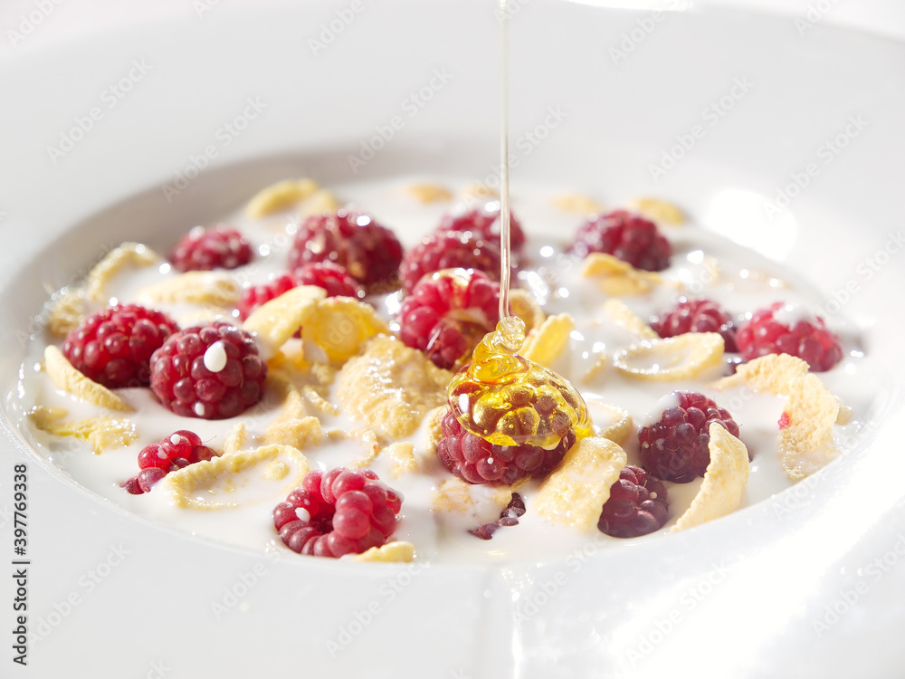 honey corn flakes with fresh raspberry and pouring milk in bowl honey corn flakes with fresh raspberry and pouring milk in bowl