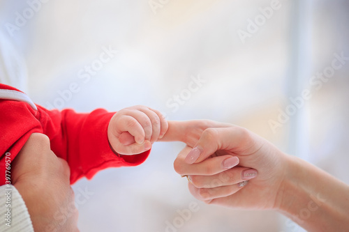 Close up Infant in santa claus suit gently holding mom finger. Baby squeezes parent hand on white background. Family and Mothers day concept. Christmas concept. Baby care. Happy childhood. copy space