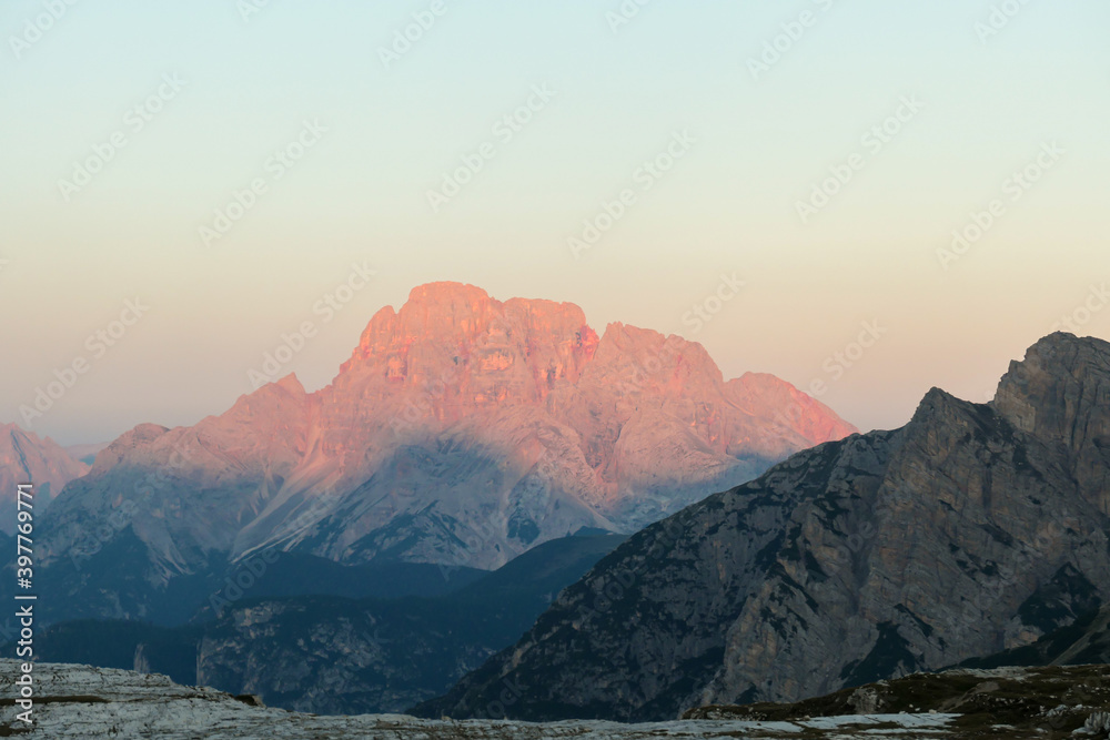 Golden hour in Italian Dolomites. The mountains are shining with pink and orange. Sunrise in high mountains. Morning haze. Lower parts of the valley still covered with shadow. New day beginning
