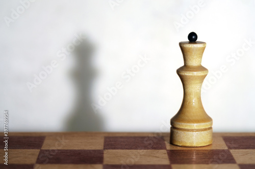 Wooden chess piece and a chessboard with drop shadows on the wall, selective focus