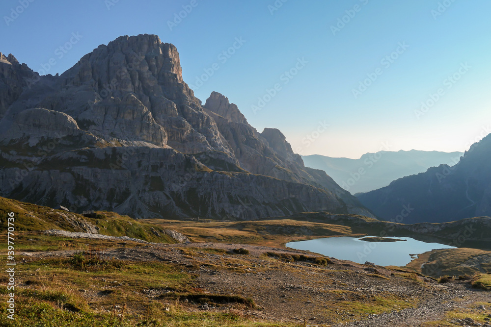 A panoramic view on a vast valley in Italian Dolomites during early morning hours. The valley is surrounded with high mountains from each side. Small lake in the middle. Remote and isolated place.