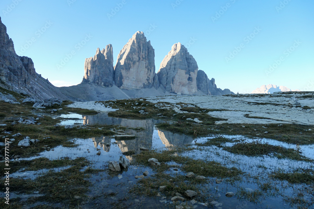 A panoramic view on the Tre Cime di Lavaredo (Drei Zinnen), mountains in Italian Dolomites. The mountains are reflecting in small paddle. Desolated and raw landscape. Early morning. Daybreak