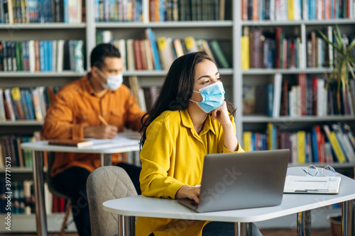 Learning during a pandemic. Students sit at a distance from each other with protective masks on their faces. A student girl sits at a desk during a lesson in a medical mask and looks away