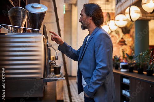 Handsome brunette man serving himself some coffee from machine