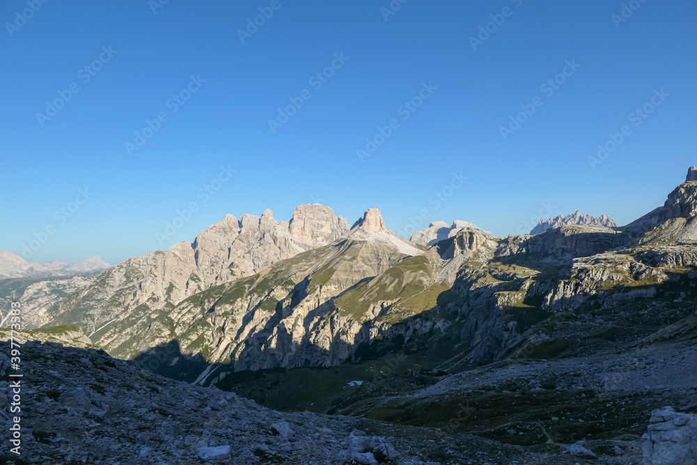 A view on a vast valley in Italian Dolomites. The valley is surrounded with high and sharp mountains from each side. Morning sun warms the valley up. Remote and isolated place. Remedy