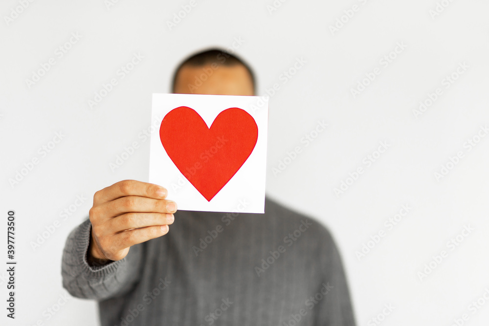 Unrecognizable man hold Valentine Copy space card. Happy Valentine's Day. Anonymous person is hiding face under greeting card in a shape of heart isolated on white background. Unrecognizable man hold Valentine Copy space card. Happy Valentine's Day. Anonymous person is hiding face under greeting card in a shape of heart isolated on white background.