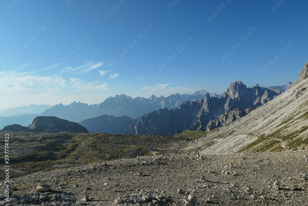 A field filled with stone men. In the back there are high chains of Italian Dolomites, shrouded in morning haze. The whole area is full of lose stones. Raw and desolated landscape. Solitude