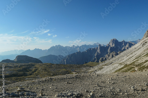 A field filled with stone men. In the back there are high chains of Italian Dolomites, shrouded in morning haze. The whole area is full of lose stones. Raw and desolated landscape. Solitude © Chris