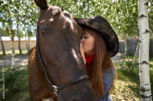 beautiful equestrian in hat hugging black horse at ranch