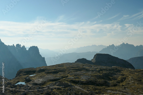 A view on a vast valley in Italian Dolomites. The valley is surrounded with high mountains from each side. Strong, early morning sun. There are a few clouds above. Remote and isolated place. Remedy