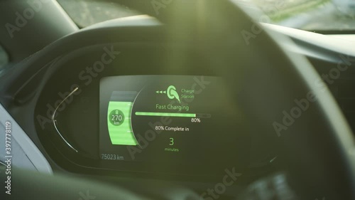 Electric car vehicle dashboard view during fast DC charging parked at power station. Green energy car interior view. Long range electric vehicle. Sunset light
