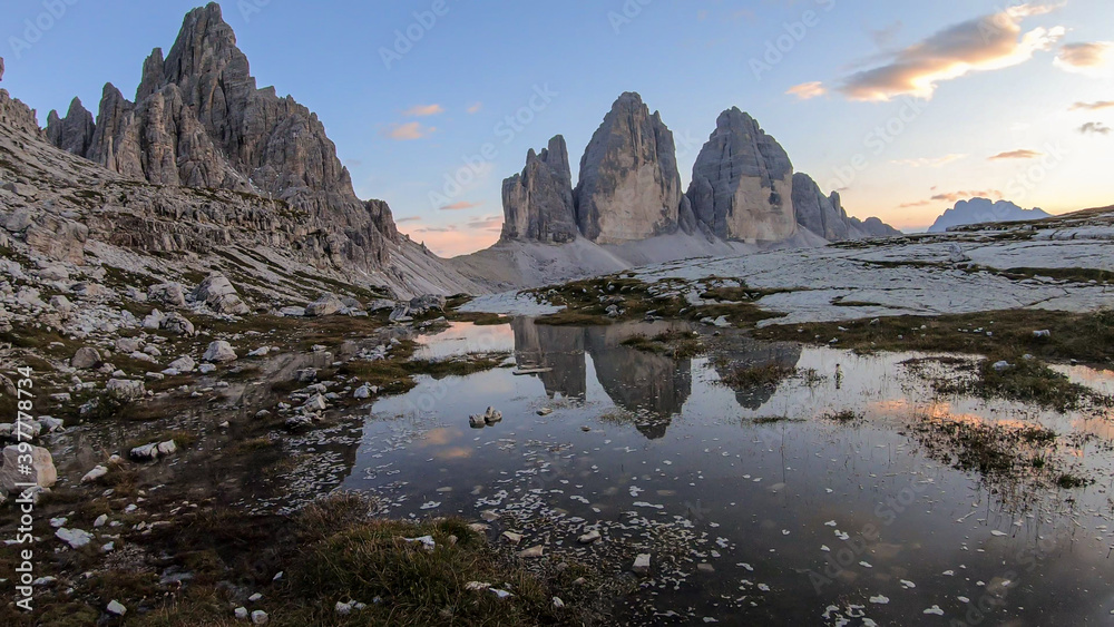 A panoramic view on the Tre Cime di Lavaredo (Drei Zinnen), mountains in Italian Dolomites. The mountains are reflecting in small paddle. Desolated and raw landscape. Early morning. Daybreak