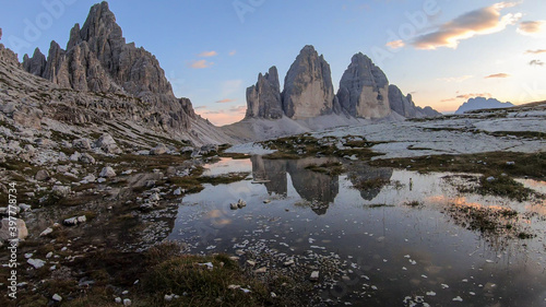 A panoramic view on the Tre Cime di Lavaredo  Drei Zinnen   mountains in Italian Dolomites. The mountains are reflecting in small paddle. Desolated and raw landscape. Early morning. Daybreak
