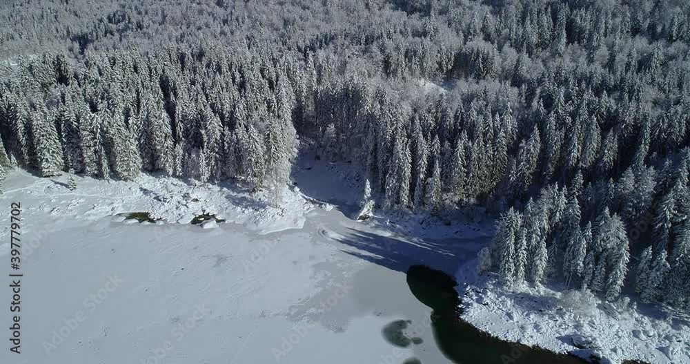 Aerial drone flying over frozen Laghi di Fusine lake in Italy. Upper superior Fusine lake in winter season. Overhead view of pristine beautiful landscape and idyll nature. Tilt up