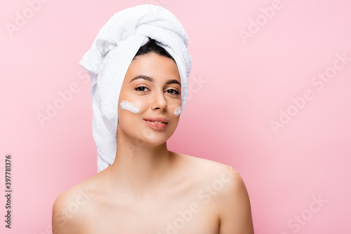 beautiful woman with towel on hair and cosmetic cream on face isolated on pink