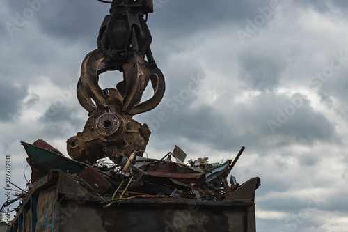 An excavator loads scrap metal into the back of a truck at a landfill or recycling center.