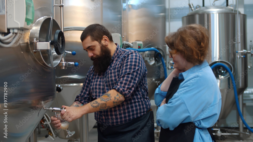 Brewery workers pourimg freshly made beer in glass tube and tasting Brewery workers pourimg freshly made beer in glass tube and tasting
