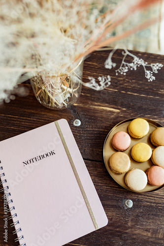 Still Life pink Notebook with Notes on dark wooden Desk with dried flowers and macarons 