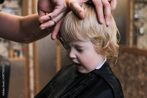 A little boy is trimmed in the barbershop. Bright emotions on the face, facial expression, the process of cutting hair.