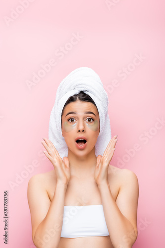 amazed beautiful woman with towel on hair and hydrogel eye patches on face isolated on pink
