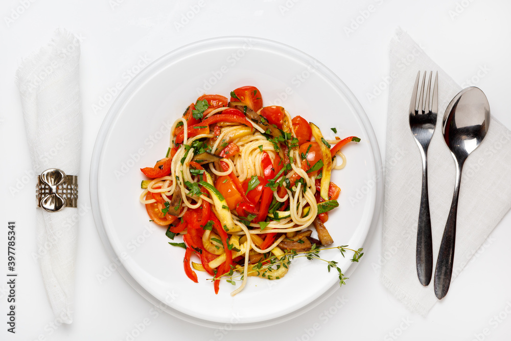 Vegetarian pasta with paprika and tomatoes on a white plate on a white wooden table, fork and spoon Vegetarian pasta with paprika and tomatoes on a white plate on a white wooden table, fork and spoon