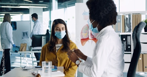 Close up portrait of African American female physician in medical mask sitting at work explaining to woman patient medicine treatment from cronavirus on medical consultation Covid-19 infection concept photo