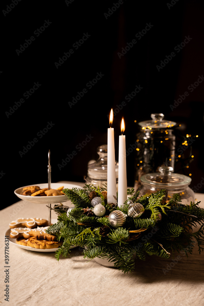 Christmas decoration: two white candles and traditional cookies arranged on linen tablecloth. Black background with copy space for text. Holidays preparation and New Year celebration concept