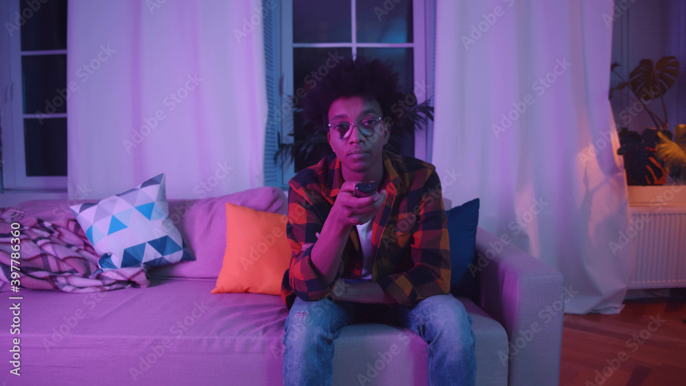 African man switching tv channels with remote control sitting on sofa at home African man switching tv channels with remote control sitting on sofa at home