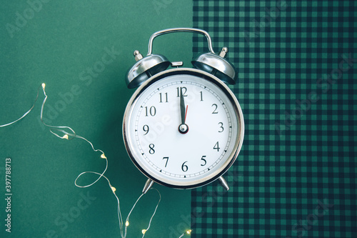 Beautiful vintage silver alarm clock and a glowing garland on a green checkered background. Time concept. Holiday routine