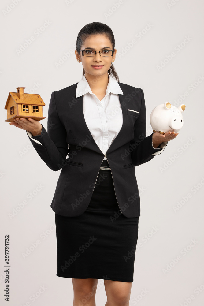 Cheerful Business woman holding piggy bank and house model on white. Cheerful Business woman holding piggy bank and house model on white.