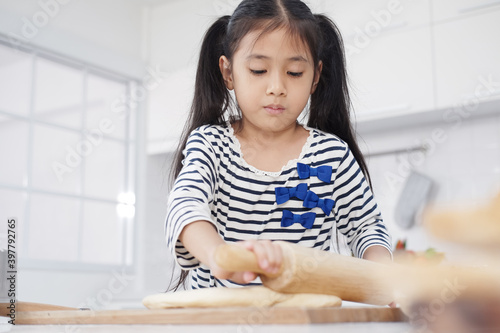 Smiling little asian girl child is Kneading the dough for baking bakery on wooden table in kitchen. Homemade pastry for bread. Family love and Homeschool Concept.