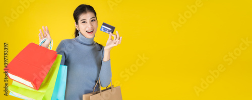 Portrait of Asian happy women holding colorful shopping bags and show credit cards,looking at camera isolated on yellow background with copy sapce,shopping and lifestyle concept.