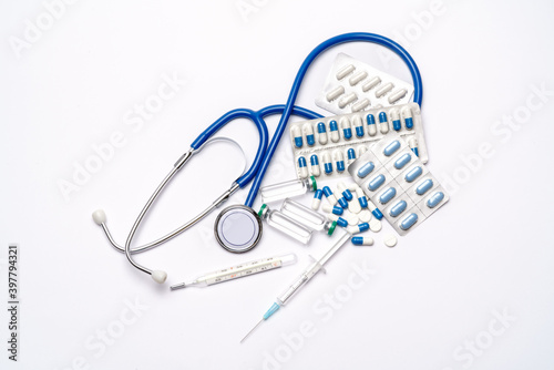 stethoscope, thermometer, syringe and capsules pills over light grey or white background - top view flat layout