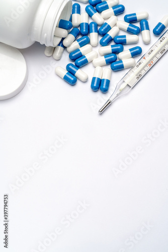 Medications capsules in a bottle and thermometer on light grey background