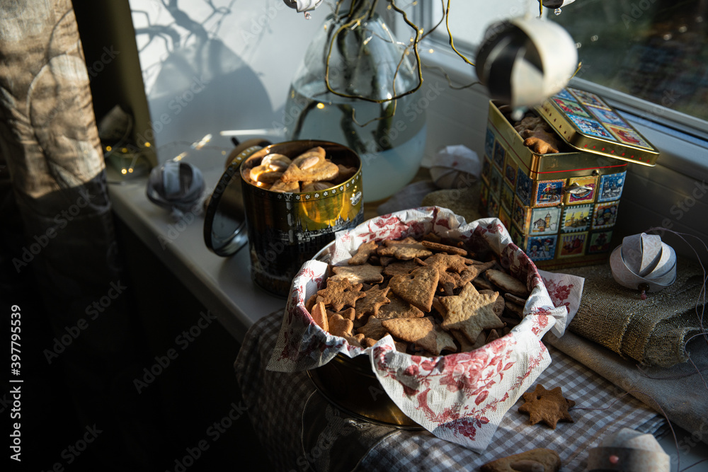 Three metal boxes with homemade Swedish pepparkakor (pepper cookies) and gingerbread cookies and willow branches decorated with Christmas ornaments on the windowsill. 