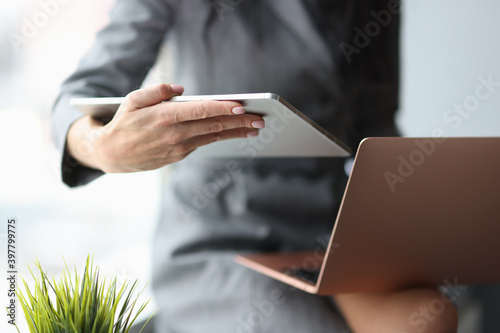 Business woman holding digital tablet and laptop in hands in office closeup