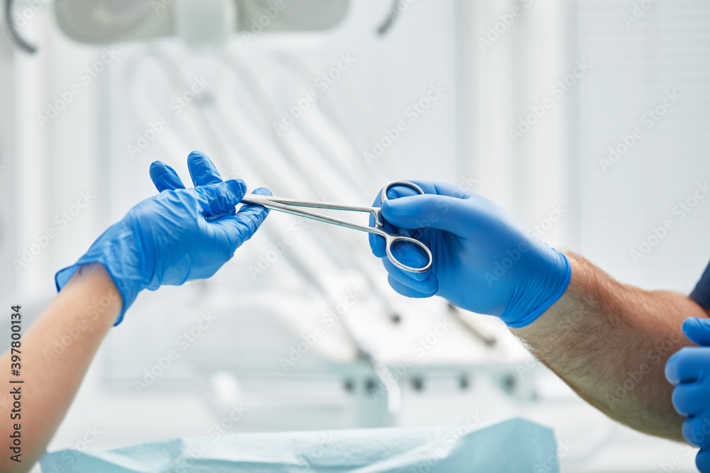 Close-up of the hands of a dentist and nurse surgeon over an operating room during a dental implant operation Close-up of the hands of a dentist and nurse surgeon over an operating room during a dental implant operation